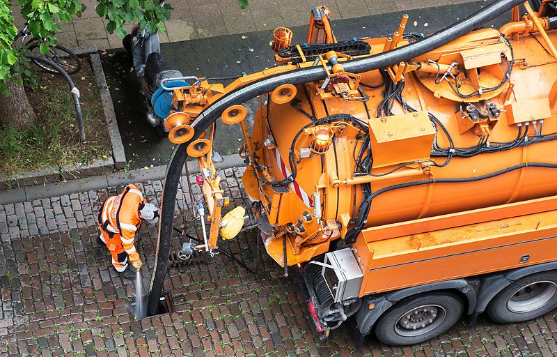 In the street, a worker cleaning a sewer with a vacuum truck, in Germany.
