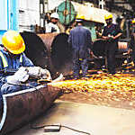 A worker is using an angle grinder, in his corner, as his co workers do their own work.