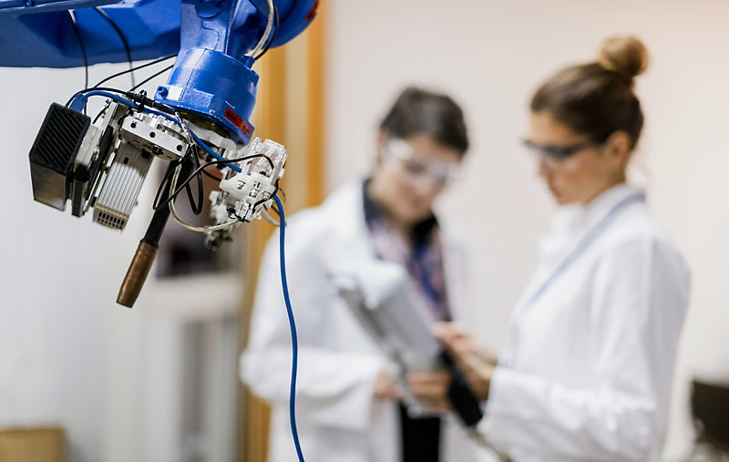 Two female engineers working with robotic a arm.