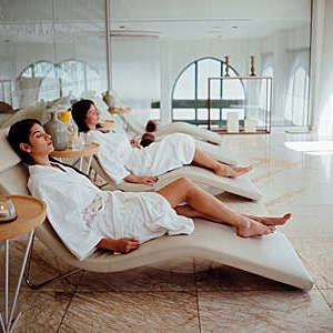 Two women in white robes relaxing at hotel spa.