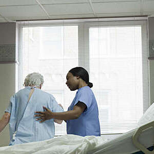Close-up of hospital nurse helping an elderly lady get out of bed.