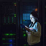 Light from a digital tablet reflects on a young girl’s face as she works in a dimly lit server room.