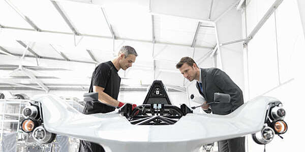 Engineer and automotive designer inspecting part-built supercar in car factory.