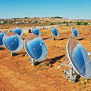 Solar Thermal Power Station with parabolic dish reflector in red dirt field, outback Australia