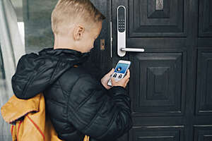 Rear view of a boy using a smartphone app to unlock the front door.